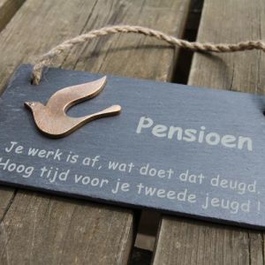 Op de foto ziet u een leistenen uithangbordje met een bronzen vogel en tekst gravure; Pensioen. Je werk is af, wat doet dat deugd. Hoog tijd voor je tweede jeugd!